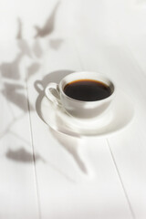 Espresso in a white cup on the table in bright sunlight. Creative composition with natural shadows. Modern breakfast. The concept of freshness of a summer morning. Minimalism, top view, white on white