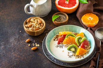 Healthy breakfast. Bowl of homemade granola with yoghurt, fresh fruit, nuts and chia seeds on a dark stone tabletop. Copy space.