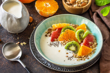 Fototapeta na wymiar Healthy breakfast. Bowl of homemade granola with yoghurt, fresh fruit, nuts and chia seeds on a dark stone tabletop.