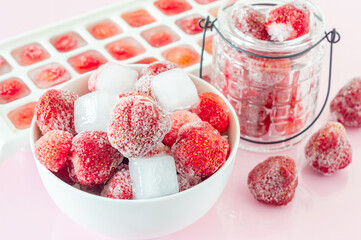 Frozen strawberry with crystals of ice on pink background