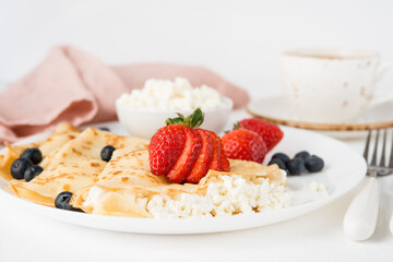 Traditional Russian thin pancakes with cottage cheese and berries in a plate on a white background