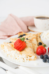 Traditional Russian thin pancakes with cottage cheese and berries in a plate on a white background, selective focus