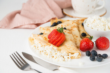 Traditional Russian thin pancakes with cottage cheese and berries in a plate on a white background, selective focus