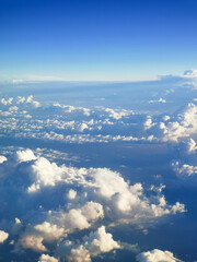 Fototapeta premium A beautiful view from an airplane on white voluminous fluffy clouds against the background of a bright blue sky, city skyscrapers below, top view, vertical frame. Beautiful natural sky background