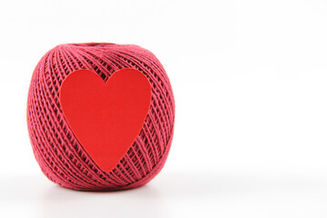 A crimson ball of thread with a red heart for crocheting on a white background. The concept of a favorite hobby of handwork, needlework and needlework. Top view. Flatlay. Copyspace.