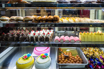 Baked cakes with colourful presentation on display in a glass food display cabinet in Chennai, Tamil Nadu, India