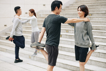 Happy young Asian couple leaning on each other when stretching quadriceps after jogging