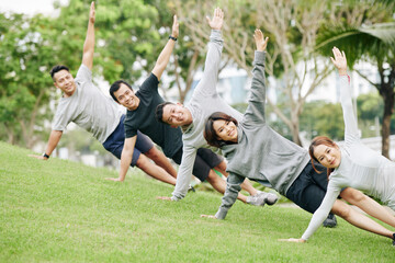 Cheerful young Vietnamese people standing in side plank and looking at camera when working out on campus or in city park
