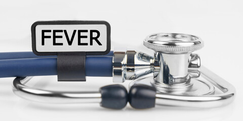 On the white surface lies a stethoscope with a plate with the inscription - FEVER