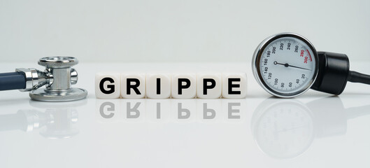 On a reflective white surface lies a stethoscope and cubes with the inscription - GRIPPE