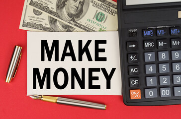 On a red background, among the money, a calculator and a pen lies a sign with the text - MAKE MONEY