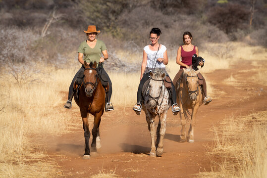 Three women ride horses along dirt track