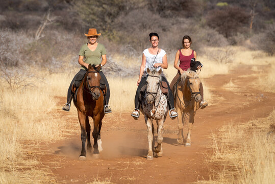 Three women ride horses on dirt track