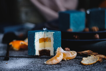 Blue cake filled with orange and tangerine in the shape of a cube. Nearby on a black table are ingredients oranges, tangerines, nuts. Rustic style.