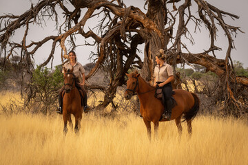 Two women on horseback by dead tree