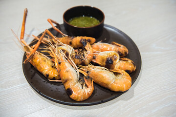 Grilled river shrimps with chili seafood sauce on black plate on wooden table.
