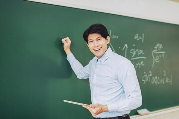 young smiling teacher standing in front of chalkboard