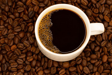 Coffee cup and coffee beans. A cup of coffee with a delicious froth surrounded by coffee beans. View from above