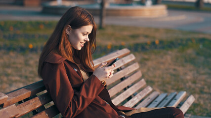 woman in the park sitting on a bench with a phone in her hands 