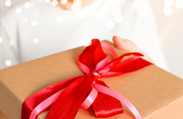 A person holds out a gift box with a bow forward, presenting a gift. Defocus lights.