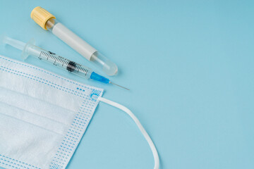 Medical syringe, face mask and blood vacuum tube on blue background with a copy space.