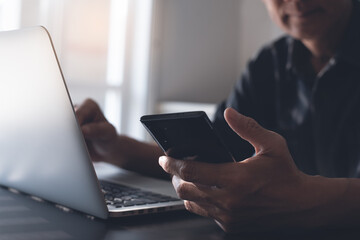 Close up of man using mobile smartphone and working on laptop computer on table office