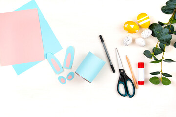 Craft making process. Scissors, colored paper, ears and paws of a rabbit on a light wooden table....