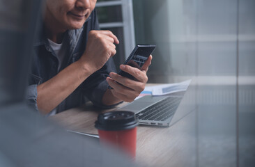 Business man using mobile phone during working on laptop computer at office