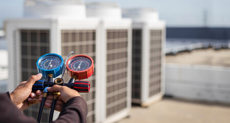 Air repair mechanic using measuring equipment for filling industrial factory air conditioners and...