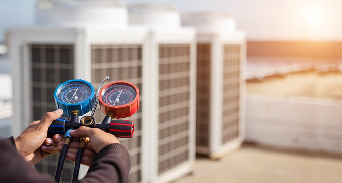 Air repair mechanic using measuring equipment for filling industrial factory air conditioners and checking maintenance outdoor air compressor unit.