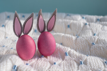 Two pink easter eggs with bunny ears close up on a white knitted blanket