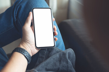 Fototapeta Mockup image of mobile smartphone with blank screen template, man sitting on sofa, hand holding and looking at mobile phone screen obraz