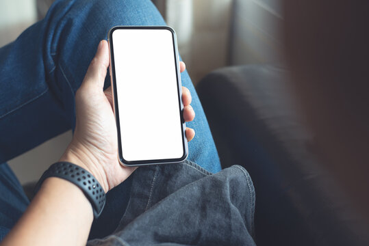Mockup image of mobile smartphone with blank screen template, man sitting on sofa, hand holding and looking at mobile phone screen