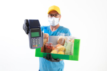 Fototapeta na wymiar Delivery guy in front of a white wall with protective mask holding box with groceries and POS for contactless payment.