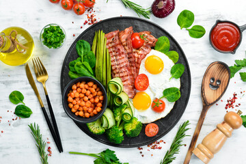 English breakfast: chickpeas, avocados, scrambled eggs, bacon vegetables on a black stone plate. Top view. Free space for text.