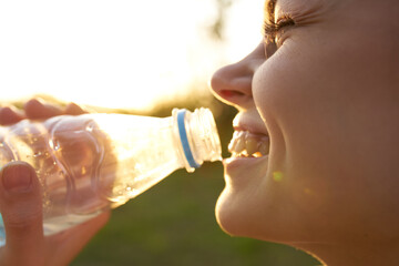 woman drinks water from a plastic bottle outdoors in summer