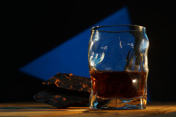 A glass of cognac and a bar of chocolate on a wooden table on a dark background