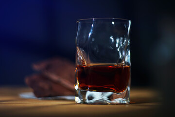 A glass of cognac and a bar of chocolate on a wooden table on a dark background