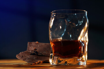 A glass of cognac and a bar of chocolate on a wooden table on a dark background