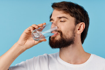 beautiful man drinking water from a glass on a blue background close-up portrait