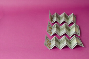 Accordion folded hundred dollar bills on a pink background.