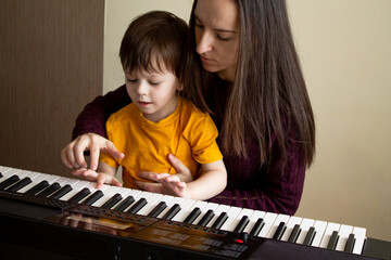 Mother teaching her son to play synthesizer. Toddler learning how to play piano. Hands on the keyboard. Early development and education concept