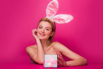 Obraz na płótnie Canvas Happy woman with gift box and bunny ears at celebration Easter, isolated on pink.