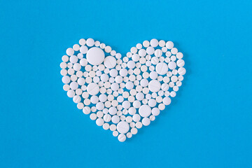 Heart made of white pills on a blue background.Various medicinal pills and capsules for health, dietary supplements and vitamins for heart health and antiviral agents. Farm drugs.