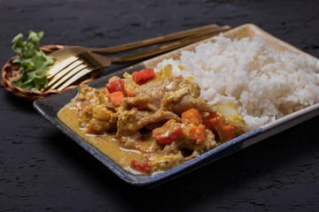 Stir fried pork curry powder with steamed rice in a plate on a black background.