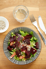 Salad with fresh beetroot, suflower seeds and grapefruits, knife, fork and water on the wooden table, no person, horizontal format