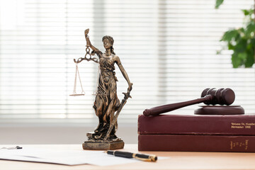 Lady Justice or Themis, books and gavel on table in bright office.