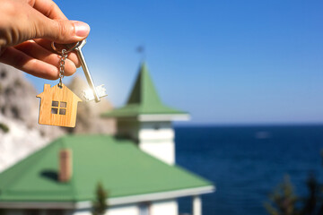 Wooden pendant of a house and key. Background of sea, fir tree and cottage. House and life on...