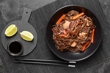 Plate with tasty soba noodles and meat on dark background