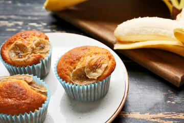 Tasty cupcakes and ripe banana on dark wooden background, closeup